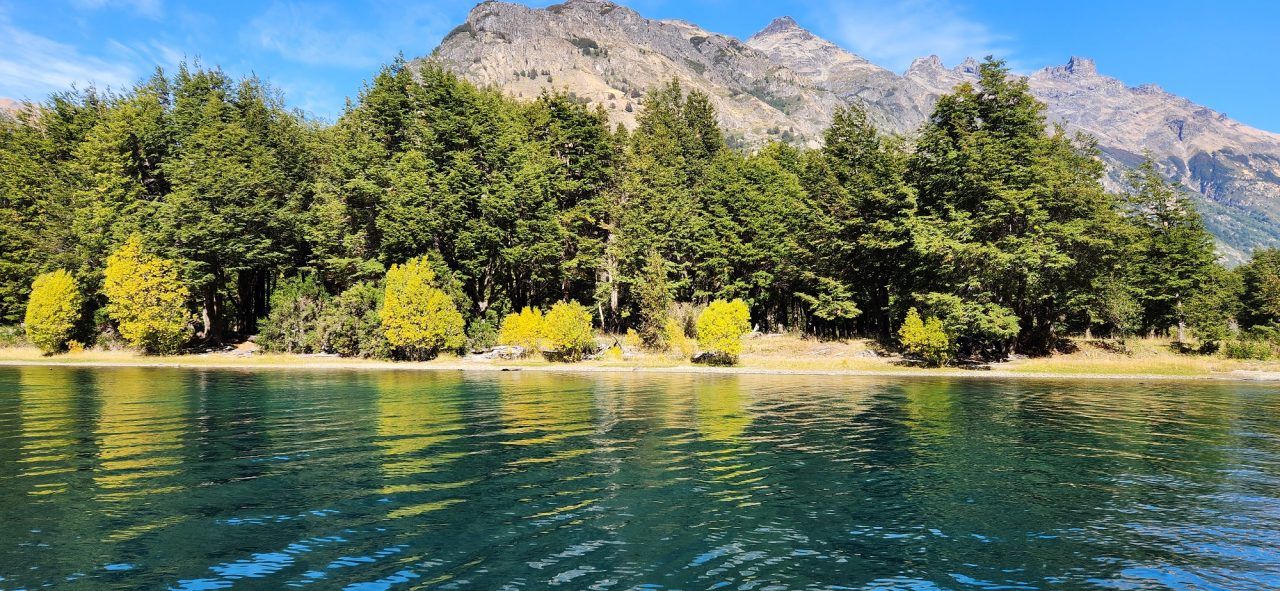 Lush green trees line the shore of Lago Azul, with a backdrop of rugged mountains.