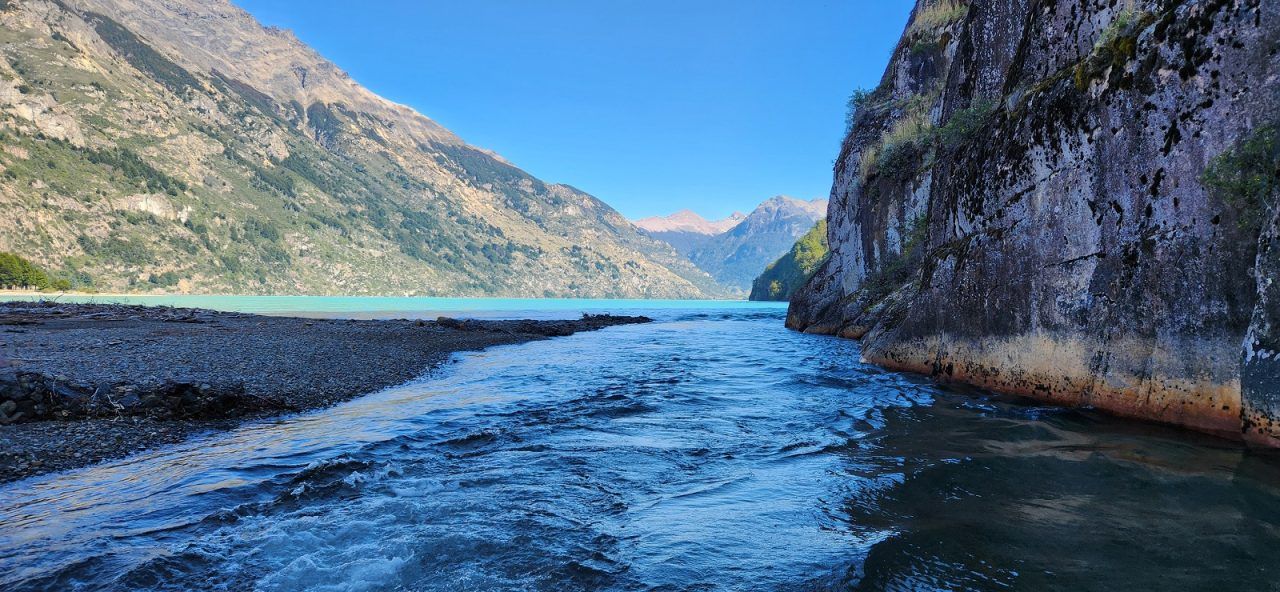 Water flows from Lago Azul, framed by rocky cliffs and mountains in the distance.
