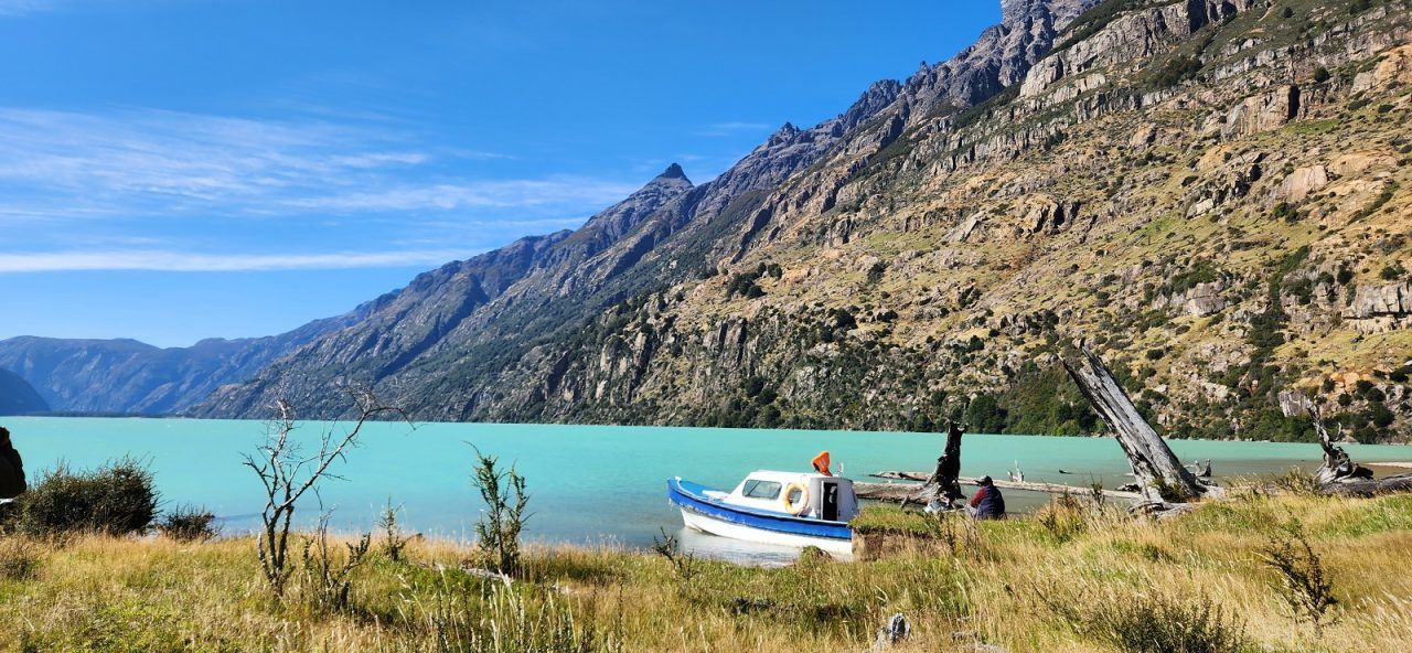Boat docked on the shore of the Coyhaique lot, with turquoise water and a mountain backdrop.